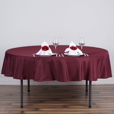 Burgundy tablecloth set for elegant dining with rose-adorned napkins and glassware.