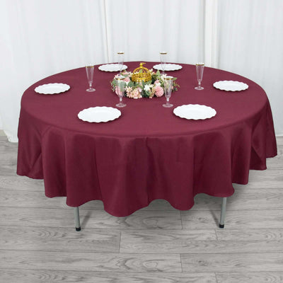 Round burgundy tablecloth with decorative table setting and white plates.
