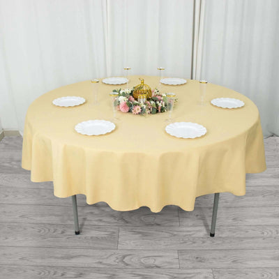 Round yellow tablecloth with decorative centerpiece and plates set for dining.