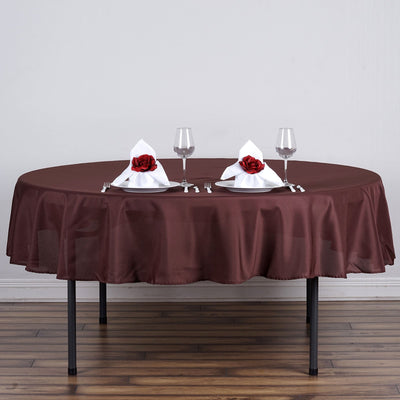 Elegant brown round tablecloth with white napkins and red rose decor.