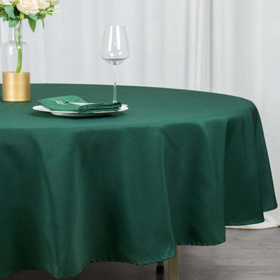 Green round tablecloth with elegant dining setup and glassware.