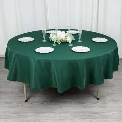Round green tablecloth on a dining table set with plates and candles.