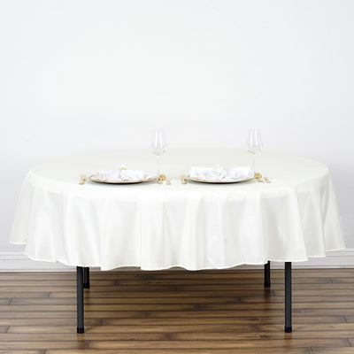 Round white tablecloth draped over a table set for two with plates and glasses.