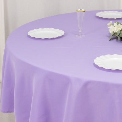 Lavender tablecloth set with white plates and a glass on a round table