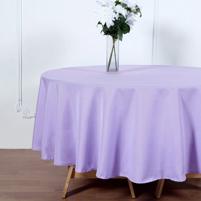 Lavender round tablecloth draped on a table with flowers in a vase.