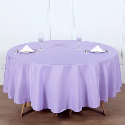 Round lavender tablecloth on a wooden table set for dining.