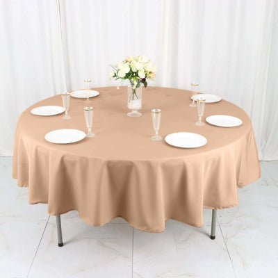 Round beige tablecloth draped over a table set with plates and glasses.