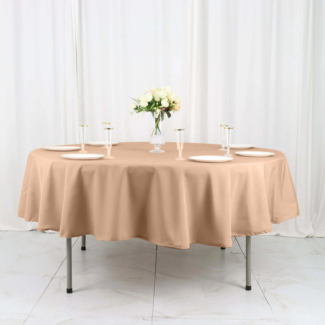 Beige round tablecloth draped over a table with plates and glasses.