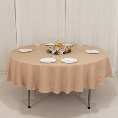 Round beige tablecloth draped over a table with plates and glasses arranged.