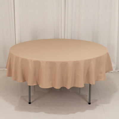 Round beige table with a smooth tablecloth on a plain backdrop