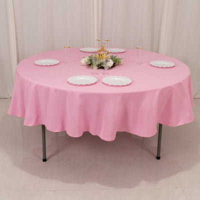 Round pink tablecloth with white plates set for dining.