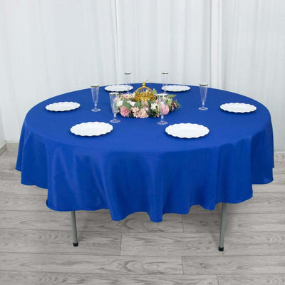 Round blue tablecloth draped over a table with plates and decorative centerpiece.