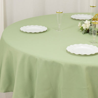 Round green tablecloth on a table set with white plates and glasses.