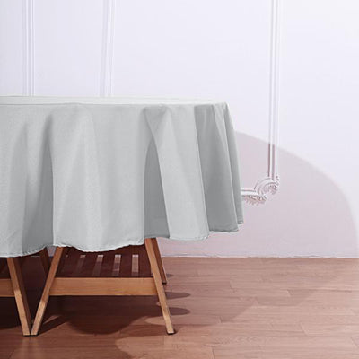 Grey round tablecloth draped over a wooden table in a staged setting.