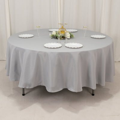 Round gray tablecloth draped on a table with plates and decorative centerpiece.