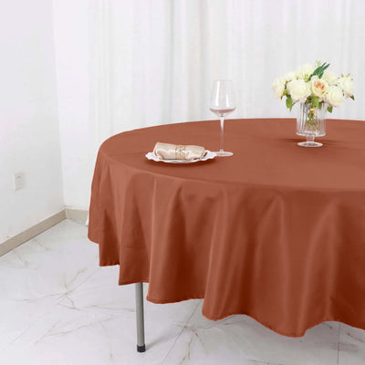 Brown tablecloth draped over a round table with a vase of flowers and a wine glass.