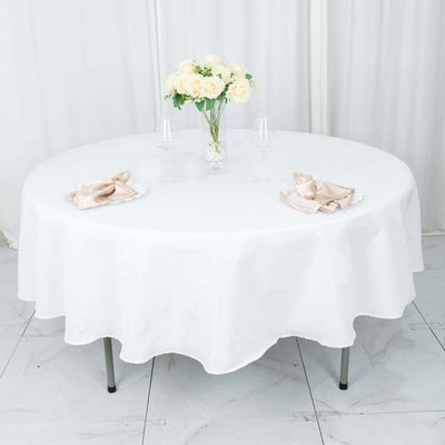 Round table set with white tablecloth, elegant napkins, and flowers.