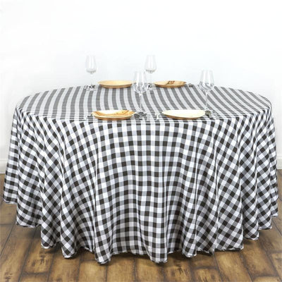 Round black and white checkered tablecloth with plates and glasses on a wooden table.