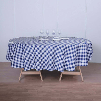 Round blue and white gingham tablecloth on a wooden table with glassware.