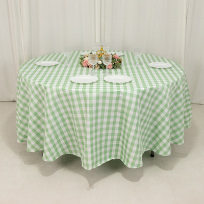 Round green checkered tablecloth set for dining with plates and floral centerpiece.