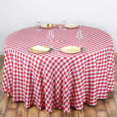 Red and white checkered round tablecloth with plates and glasses set on a wooden table.