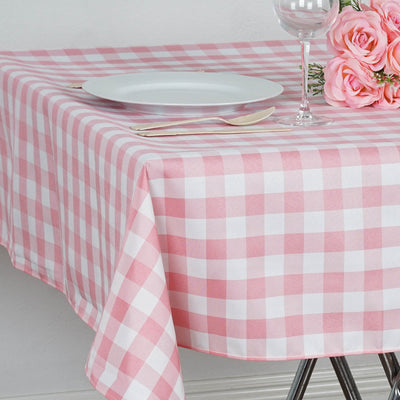 Pink and white checkered tablecloth on a dining table with a plate and flowers.