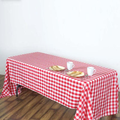 Red and white checkered tablecloth on a wooden table with plates and cups.