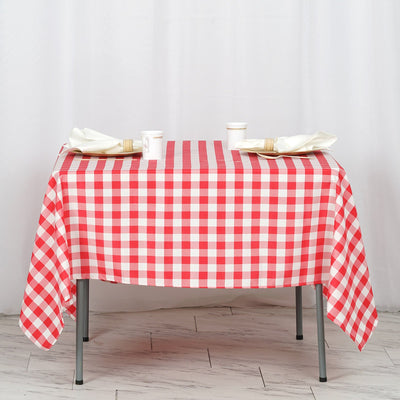 Red and white checked tablecloth on a table with utensils and cups.