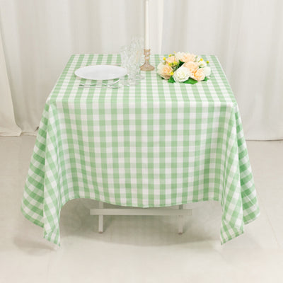 Green and white checkered tablecloth on a dining table with flowers and plates.