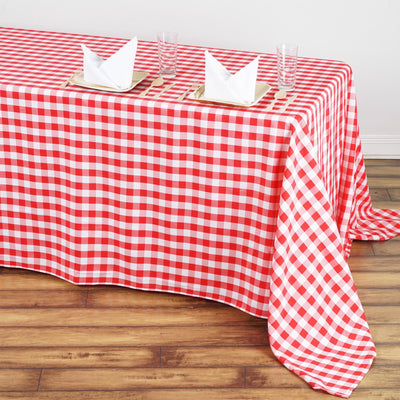 Red and white checkered tablecloth on a wooden floor with napkins and glasses.