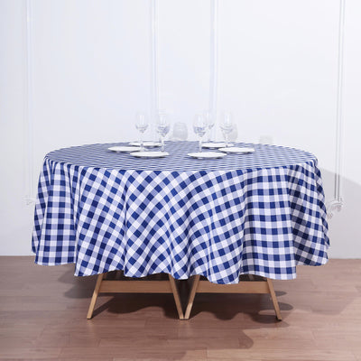 Round blue and white checkered tablecloth on a wooden table with glassware.
