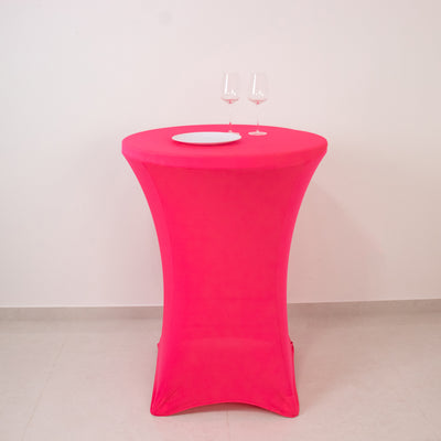 Pink table with a round top and two wine glasses on a plain backdrop.