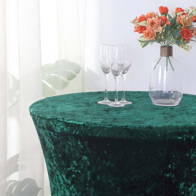 Green velvet tablecloth with glasses and a vase of flowers on a table.