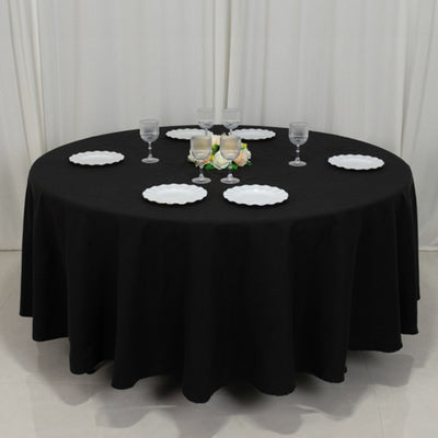 Round black tablecloth with white plates and glasses set for dining.