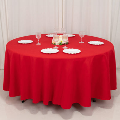Red round tablecloth with plates and glasses for dining setup.