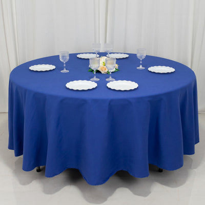 Round blue tablecloth with white plates and glasses set for dining.