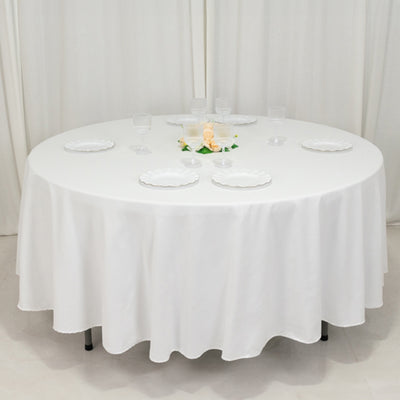 Round table with a white tablecloth set for dining, featuring clear glasses and plates.
