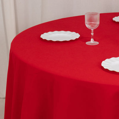 Red round tablecloth with white plates and glassware set for dining.