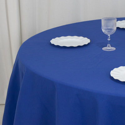 Blue tablecloth with white plates and glass on a round table.
