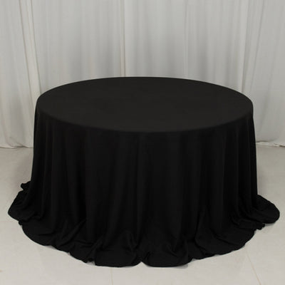 Black round tablecloth with elegant draping on a plain backdrop.