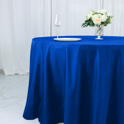 Blue tablecloth draped over a round table with a glass and floral centerpiece.