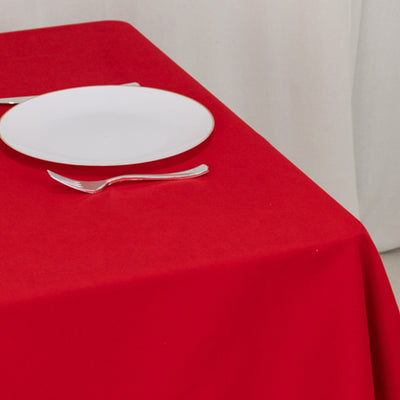 Red tablecloth with white plate and silverware on a table.