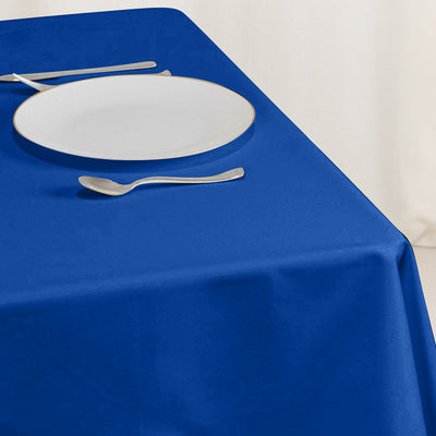 Blue tablecloth with a white plate and silver utensils on a dining table.