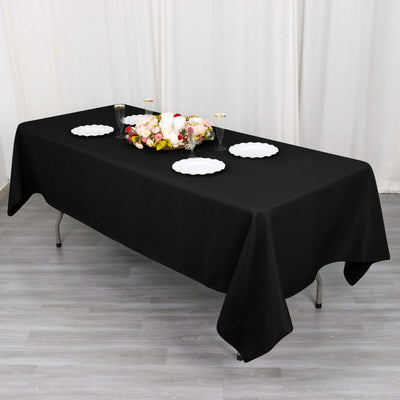Black tablecloth on a dining table set with white plates and a floral centerpiece.