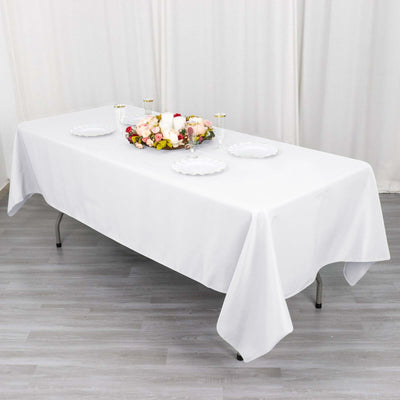 White tablecloth draped over a table set for an event with floral centerpiece.