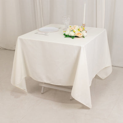White tablecloth draped over a table with flowers and candle.