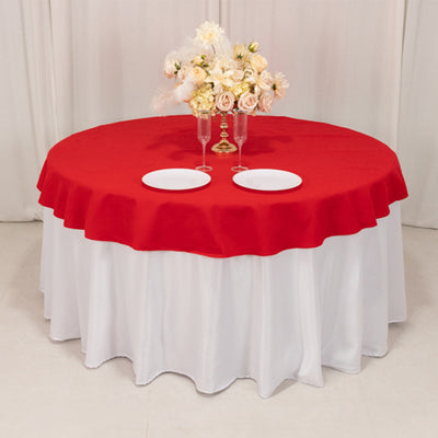 Red tablecloth on a round table with floral centerpiece and plates.