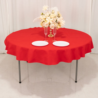 Red round tablecloth with plates and floral centerpiece on a table.