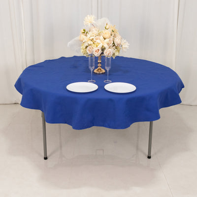 Round blue tablecloth draped over a table with plates and flowers.