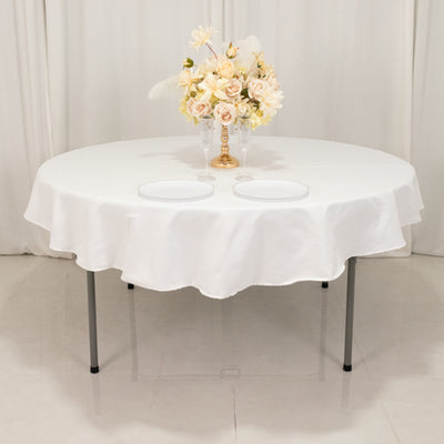 Round table dressed in a white tablecloth with plates and floral centerpiece.